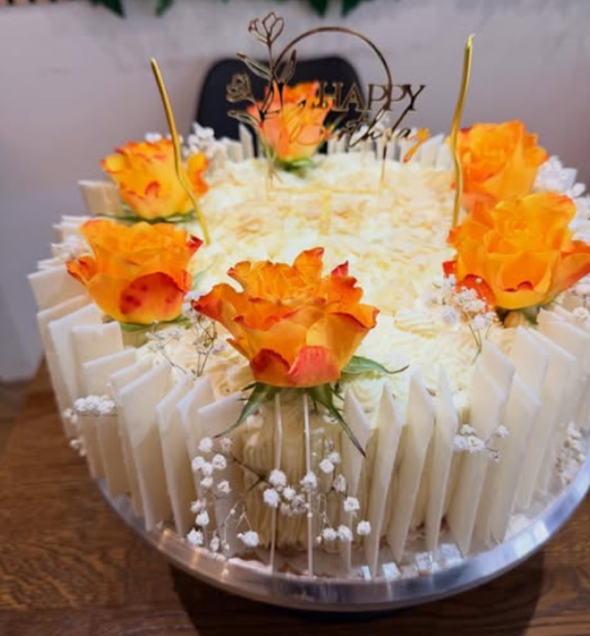 Weiße Geburtstagstorte mit orangen Rosen und Schokoladen-Blättern